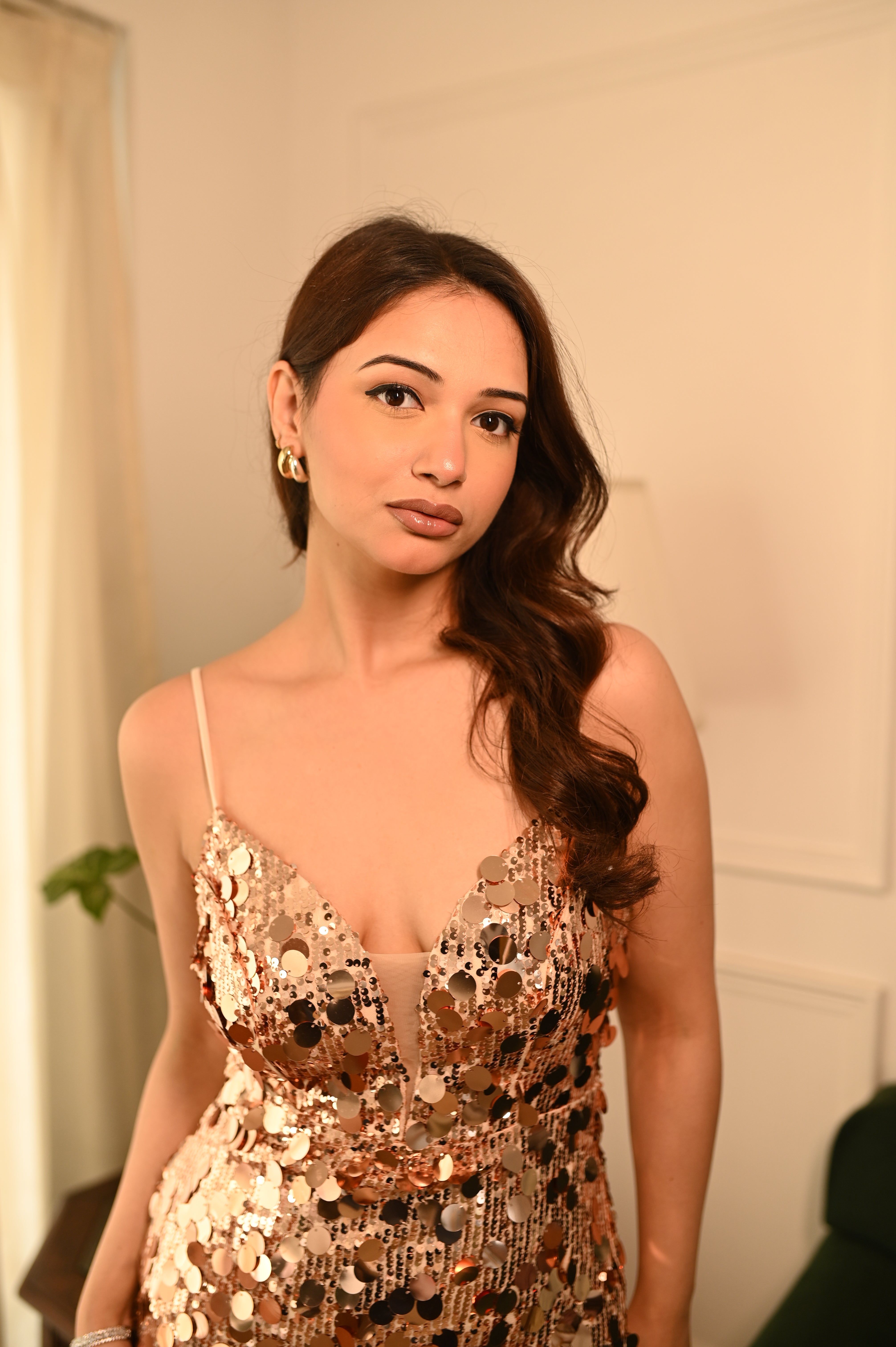 Woman in a sequinned gold dress by niyara india posing indoors