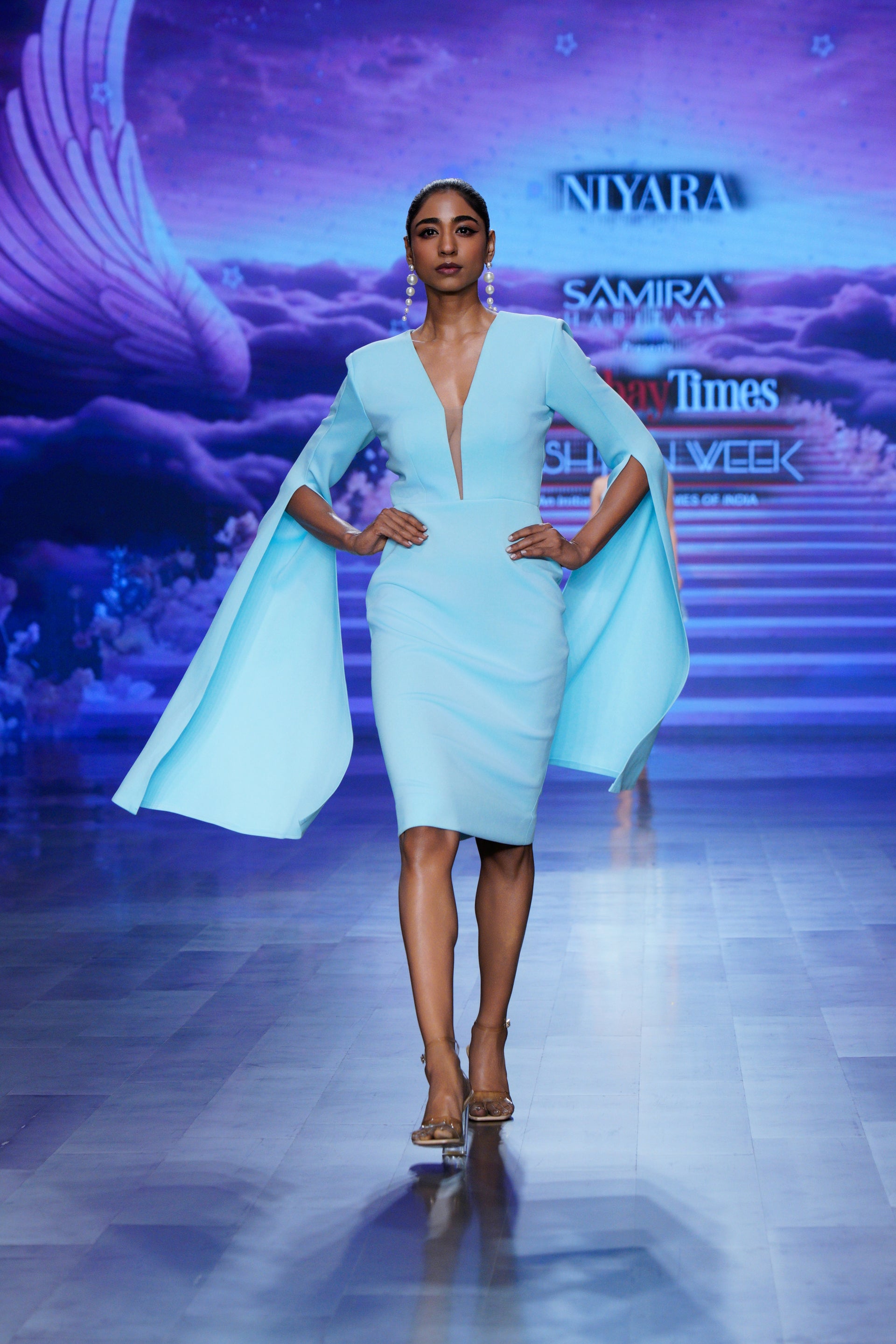 woman in a light blue cape midi dress walking the ramp